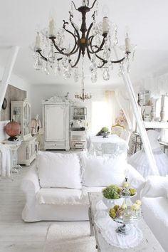 a living room filled with white furniture and a chandelier hanging from the ceiling