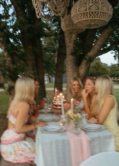 three women sitting at a table with a cake in front of them and candles on the table