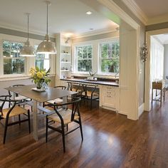 a dining room and kitchen area with hardwood floors, white walls, and large windows