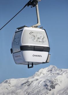 a cable car with the word chanel painted on it's side in front of snow covered mountains