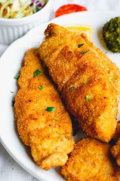 some fried food on a white plate with broccoli and coleslaw in the background