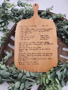 a wooden cutting board sitting on top of a wreath filled with green leaves and plants