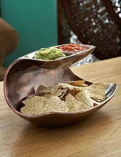 a wooden table topped with a metal bowl filled with chips and guacamole