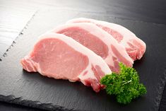 two raw pork chops sitting on top of a black cutting board with parsley