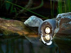 a light that is sitting on top of some rocks in the water with grass behind it