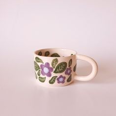 a coffee cup with purple flowers painted on the outside and green leaves on the inside