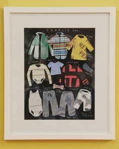 a framed photo of baby's clothes hanging on a wall in front of a yellow frame