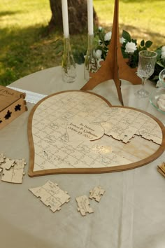 a heart shaped wooden puzzle sitting on top of a table next to candles and flowers