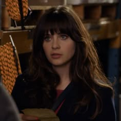 a woman with long brown hair and bangs standing in front of stacks of orange objects