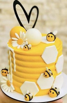 a yellow cake with bees and honeycombs on it, topped with a heart