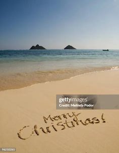 the word christmas written in sand on a beach with two small islands in the background