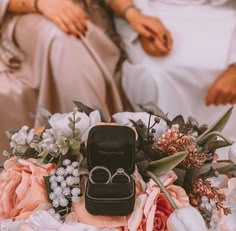 two people sitting next to each other with wedding rings on top of the flower bouquet