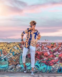 a man standing in front of a graffiti wall with his hands on his hips while wearing white pants