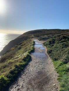 a dirt path leading to the top of a hill next to the ocean on a sunny day