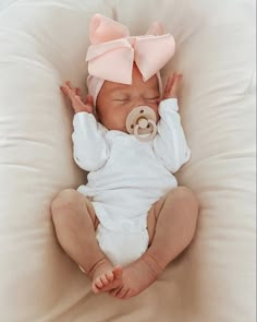 a baby with a pacifier in its mouth laying on a pillow wearing a pink bow