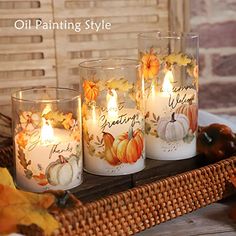 three candles sitting on top of a basket filled with pumpkins and other autumn decorations