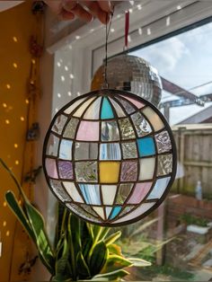 a stained glass ball hanging from the ceiling in front of a potted plant and window