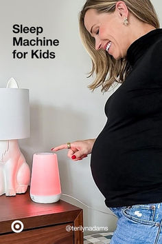 a pregnant woman pointing at a pink light next to a night stand with a cat lamp on it