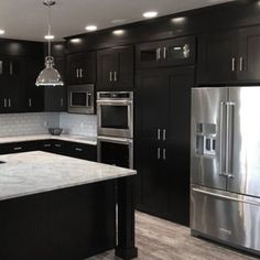 a large kitchen with black cabinets and stainless steel appliances, along with marble counter tops