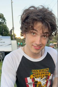 a young man with curly hair is posing for the camera in front of an rv park