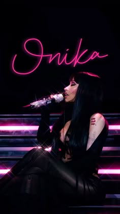 a woman with long black hair sitting on a bench and holding a microphone in her hand