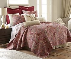 a bed with red and white comforters in a room next to a window,