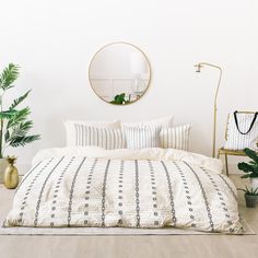 a bedroom with white walls and wooden flooring has a round mirror above the bed