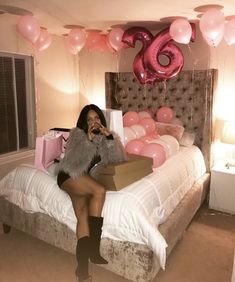 a woman sitting on a bed with pink balloons and presents in front of her face