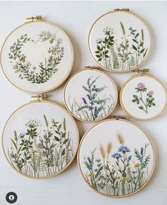 four cross stitch embroiderys with flowers and plants in them on a white table top