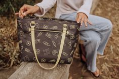 a woman sitting on a tree stump holding a brown and tan bag with symbols all over it