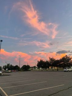 an empty parking lot with cars parked in it and the sky is pink, orange and blue