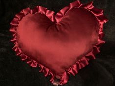 a red heart shaped pillow with ruffled edges on a black velvet surface, in the shape of a heart