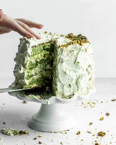 someone is cutting into a cake with white frosting and pistachio sprinkles