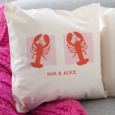 two pillows with lobsters on them sitting next to each other in front of a pink blanket