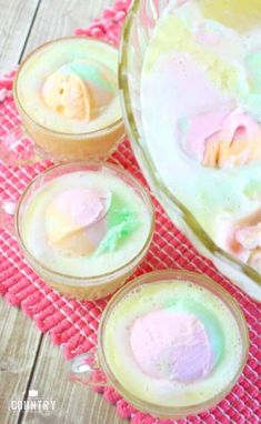 three glasses filled with different colored jello on top of a pink place mat next to a glass bowl