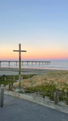 a wooden cross sitting on the side of a road next to the ocean at sunset