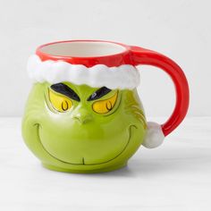 a green grin face mug with a red handle and santa's hat on it