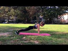 a woman is doing push ups on a pink mat in the middle of a park