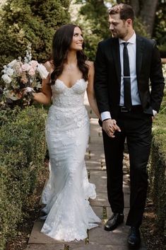 a bride and groom walking down a path holding hands