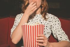 a woman eating popcorn while sitting on a red couch