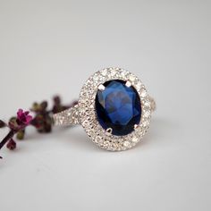 "A ring style of the royalties, this design flaunts an oval synthetic blue stone, surrounded by 0.66cts of double natural diamond halo. Crafted in solid 14k gold, the shank tapers and has diamonds enhancing the overall look. * Center Stone : Blue Sapphire Imitation (for natural, please message) * Shape : Oval (10x8 mm) * Halo Gemstones : Natural Genuine Diamonds * Diamond Wt. : 0.66 Cts * Color/Clarity : H-I, Vs-Si * Gold - 14kt, 5.9 gms solid white gold (approx) If you like this ring, please pr Blue Oval Diamond Halo Ring, Oval Blue Diamond Halo Ring, Elegant Blue Halo Ring With Lab-created Sapphire, Luxury Sapphire Oval Halo Ring, Luxury Oval Sapphire Halo Ring, Elegant Halo Ring With Lab-created Sapphire Gemstone, Luxury Blue Oval Cluster Ring, Blue Oval Halo Ring With Center Stone, Luxury Blue Oval Halo Ring