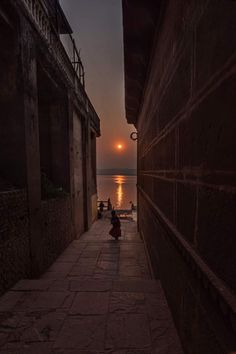 a person sitting on the side of a road next to water at night with the sun setting in the distance