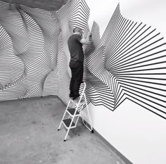 a man standing on a ladder in front of a wall with an abstract design painted on it