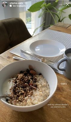 a bowl of oatmeal with nuts in it on a table next to a cup of coffee