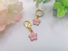 two pink flowers are attached to gold - plated keychains on a white surface