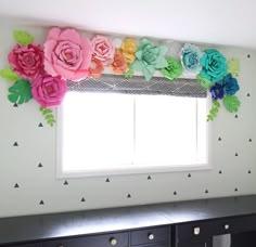 there is a window with paper flowers on the valance and black drawers below it