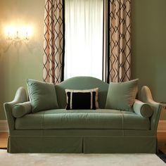 a green couch sitting in front of a window next to a table with a lamp on it