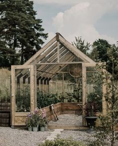 a small wooden greenhouse with plants growing in the ground and on top of graveled area