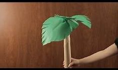 a person holding a green paper palm tree on a wooden stick in front of a wall