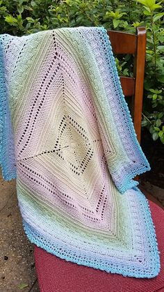 a crocheted blanket sitting on top of a wooden chair next to a bush